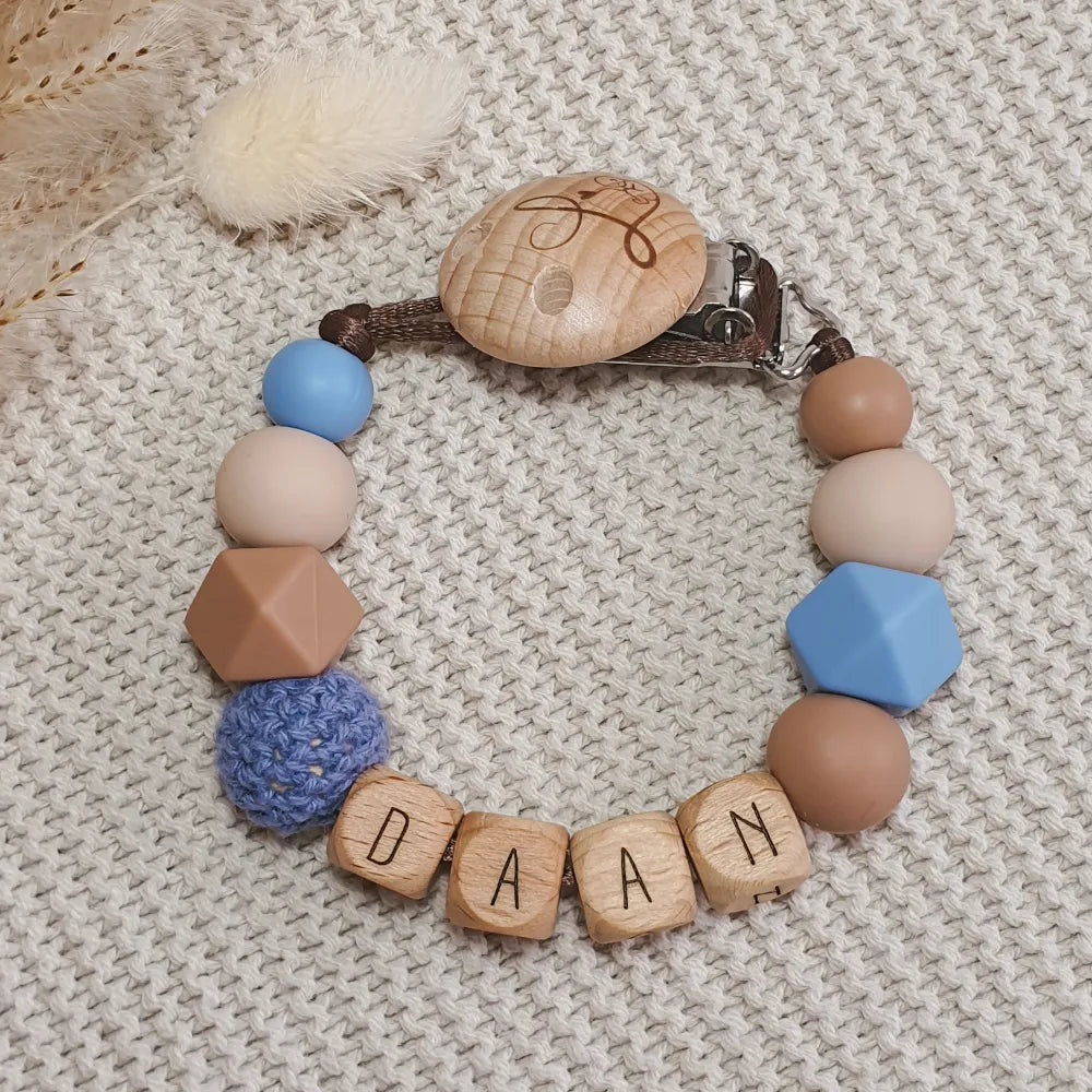 Gepersonaliseerd speenkoord met naam van houten letterkralen en siliconen kralen in blauw, bruin en beige.