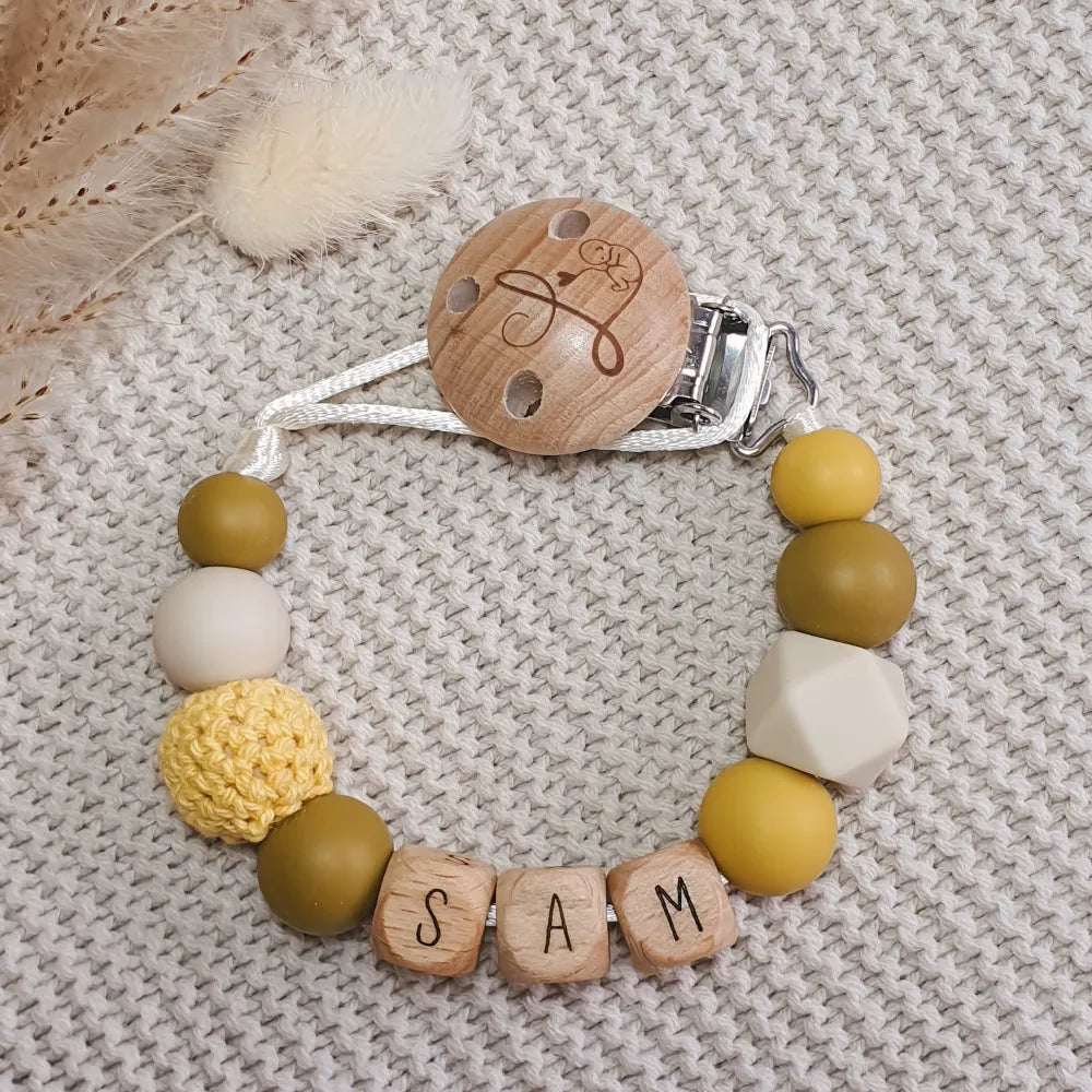 Gepersonaliseerd speenkoord met naam van houten letterkralen en siliconen kralen in geel, oker en licht beige.