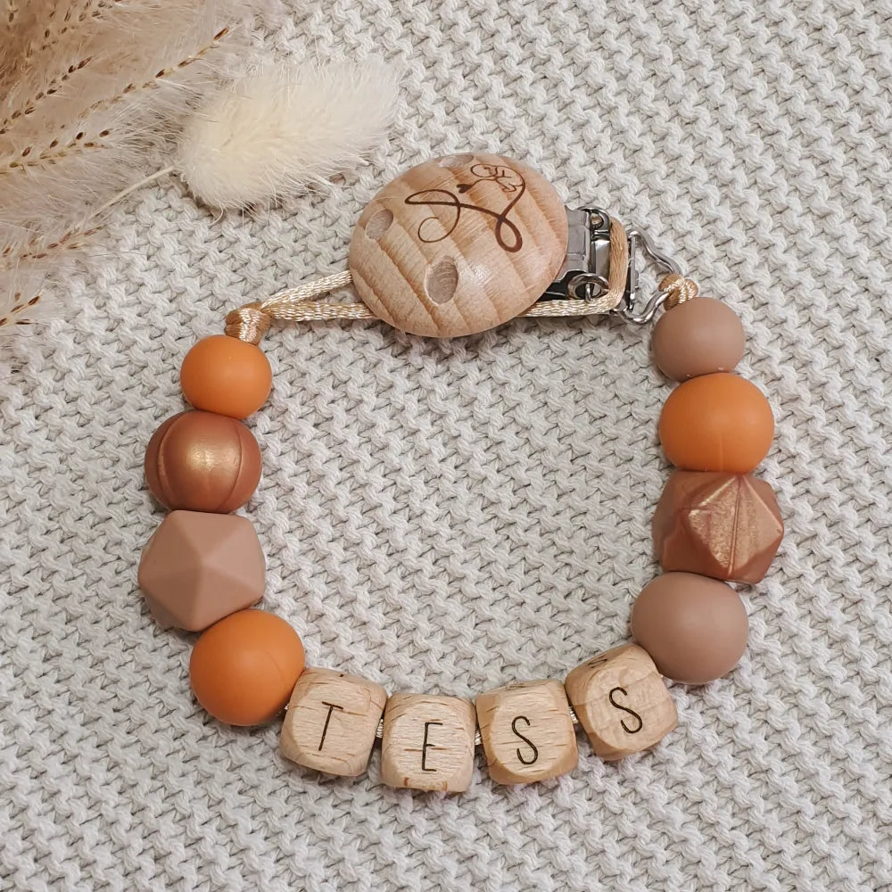 Gepersonaliseerd speenkoord met naam van houten letterkralen en siliconen kralen in oranje, bruin en koper.