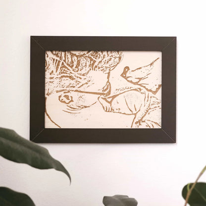 Een op hout gegraveerde foto van een vader met pasgeboren zoon in een donkere omlijsting.