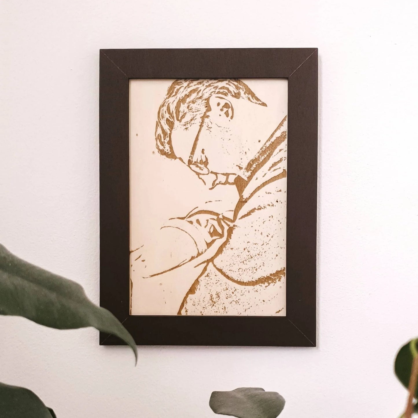 Een op hout gegraveerde foto van een vader met pasgeboren zoon in een donkere omlijsting.