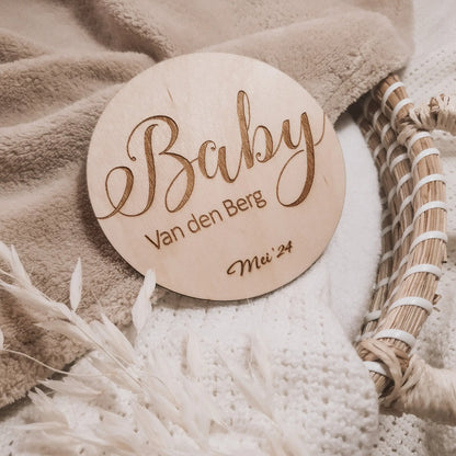Houten aankondigingsbordje voor een zwangerschap, gegraveerd met de achternaam en uitgerekende datum.
