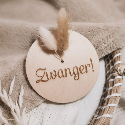 Houten aankondigingsbordje met droogbloemen voor een zwangerschap, gegraveerd met de tekst "zwanger".