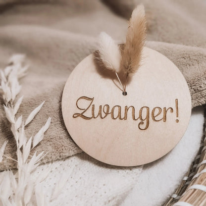 Houten aankondigingsbordje met droogbloemen voor een zwangerschap, gegraveerd met de tekst "zwanger".