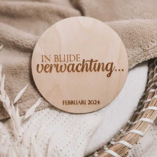 Houten aankondigingsbordje voor een zwangerschap, gegraveerd met de tekst "In blijde verwachting" en de uitgerekende datum.