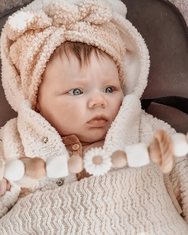 Babymeisje in een kinderwagen met een wagenspanner van siliconen kralen en houten details.