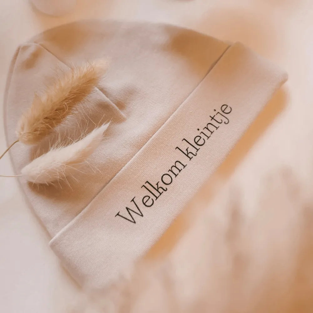 Beige babymutsje voor pasgeboren baby's, bedrukt met de tekst "Welkom kleintje".