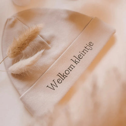 Beige babymutsje voor pasgeboren baby's, bedrukt met de tekst "Welkom kleintje".