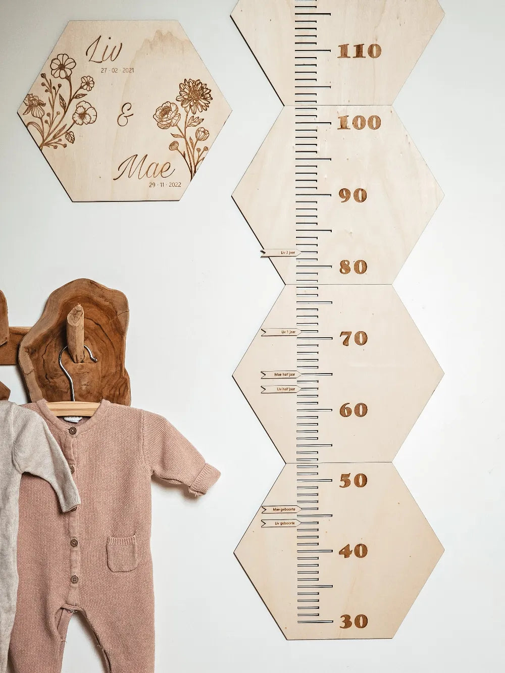 Houten groeimeter met naam in hexagon-vorm met geboortebloemen aan de muur van een kinderkamer.
