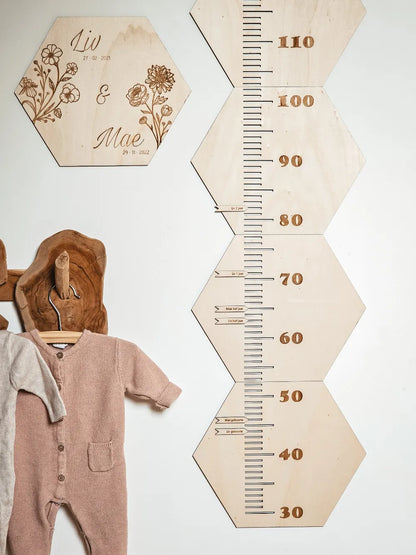 Houten groeimeter met naam in hexagon-vorm met geboortebloemen aan de muur van een kinderkamer.