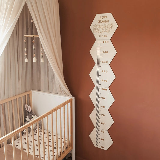 Houten groeimeter met naam in hexagon-vorm van 150cm hoog aan de muur van een babykamer.
