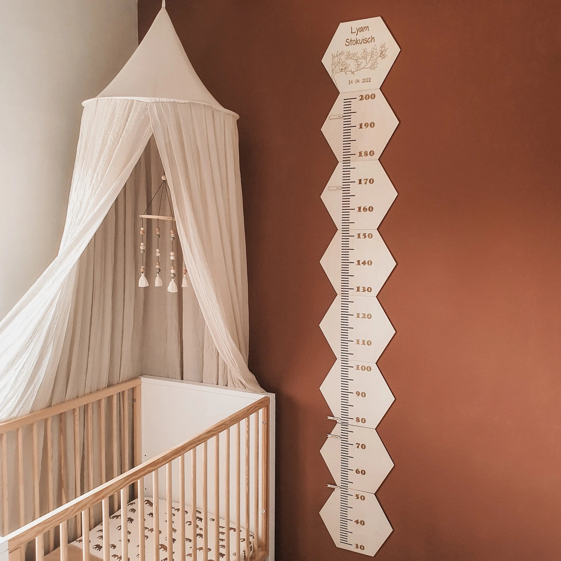 Houten groeimeter met naam in hexagon-vorm van 200cm hoog aan de muur van een babykamer.