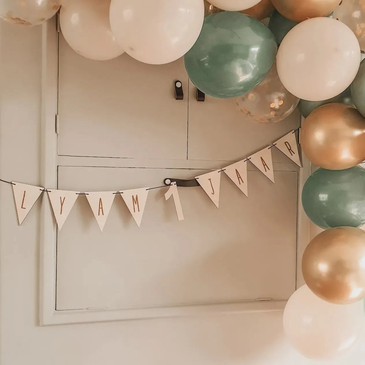 Houten vlaggenlijn met naam en leeftijd voor een verjaardag, omringt met ballonnen.