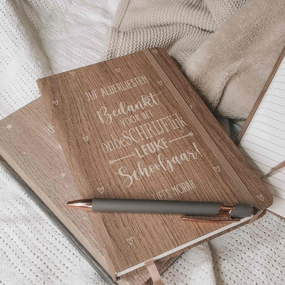 Gegraveerde notitieboekjes in verschillende kleuren houtlook voor meesters en juffen met de tekst 'Bedankt voor het onbeschrijflijk leuke schooljaar'.