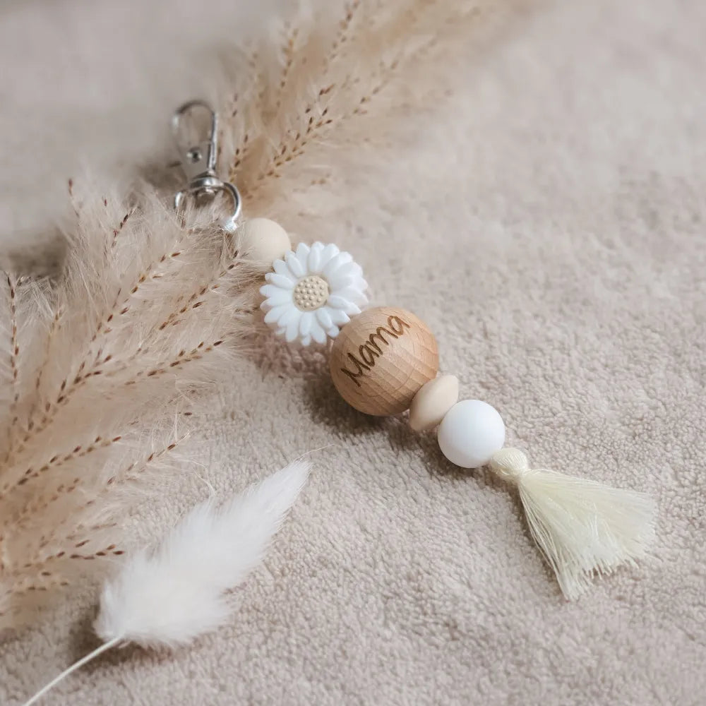 Sleutelhanger met witte en beige siliconen kralen, een witte bloem en kwastje en 'mama' gegraveerd op een houten kraal.