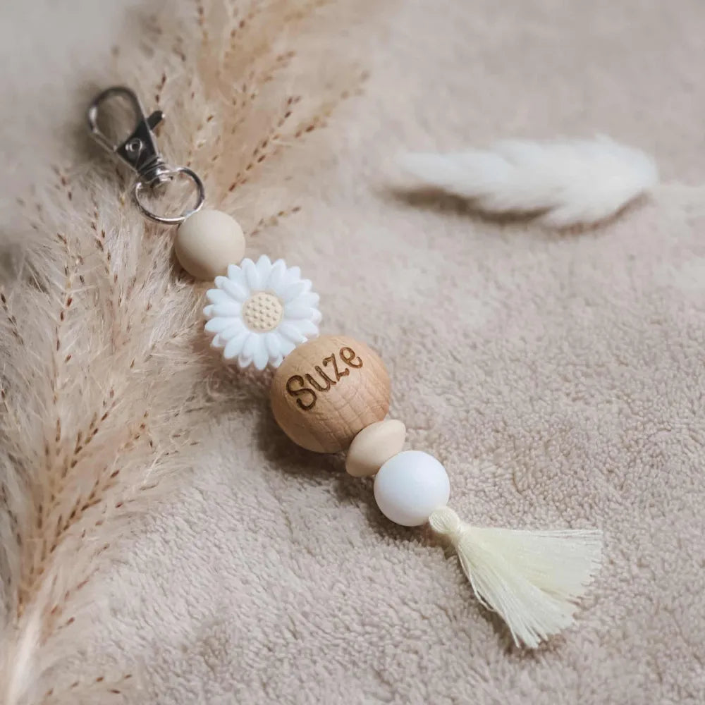 Gepersonaliseerde sleutelhanger met witte en beige siliconen kralen, een witte bloem en kwastje en de naam gegraveerd op een houten kraal.