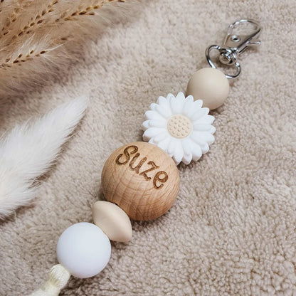 Gepersonaliseerde sleutelhanger met witte en beige siliconen kralen, een witte bloem en kwastje en de naam gegraveerd op een houten kraal.