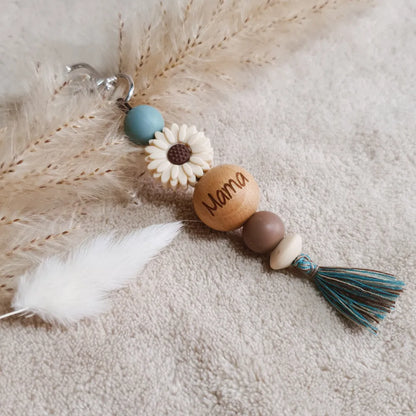 Sleutelhanger met blauwe en bruine siliconen kralen, een beige bloem en een kwastje, met 'mama' gegraveerd op een houten kraal.
