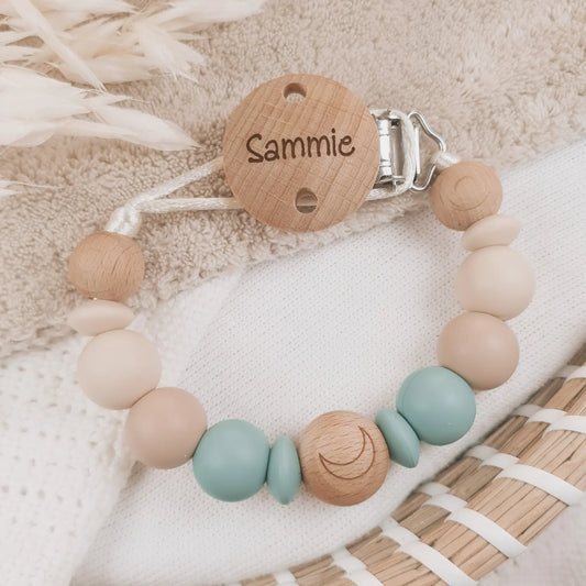 Gepersonaliseerd speenkoord met naam gegraveerd op de clip en siliconen kralen in beige en blauw met houten details.