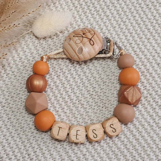 Gepersonaliseerd speenkoord met naam van houten letterkralen en siliconen kralen in oranje, bruin en koper.