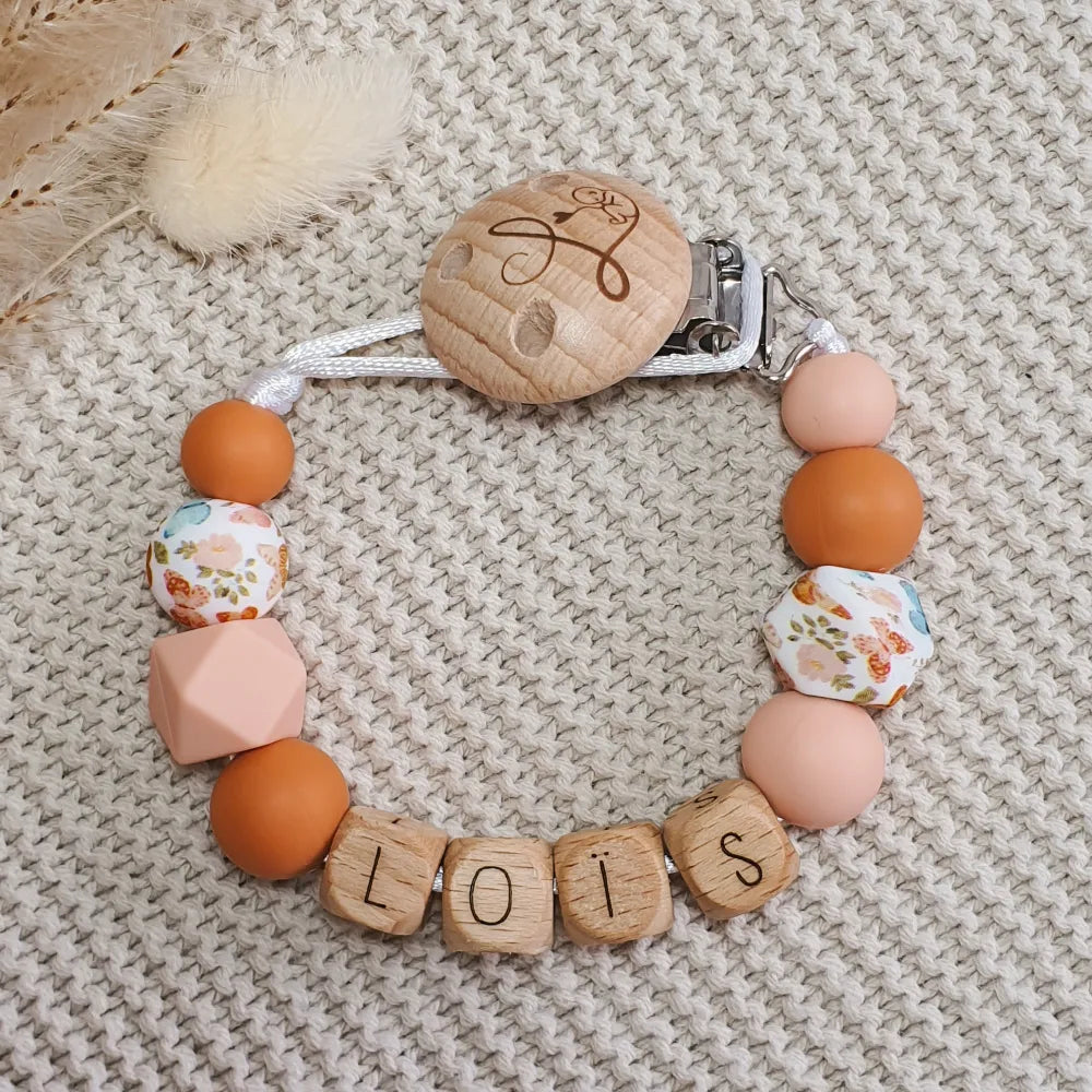 Gepersonaliseerd speenkoord met naam van houten letterkralen en siliconen kralen in oranje, roze en vlinder-print.