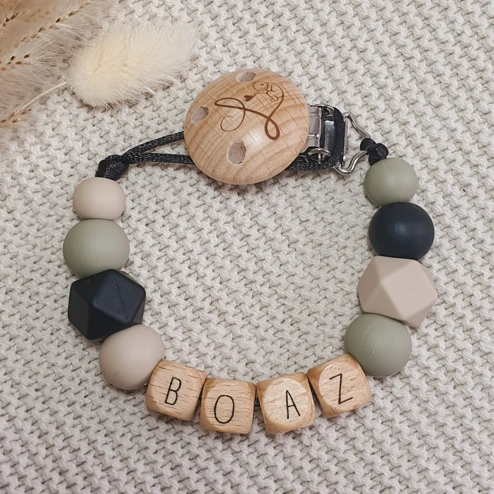 Gepersonaliseerd speenkoord met naam van houten letterkralen en siliconen kralen in groen, zwart en beige.