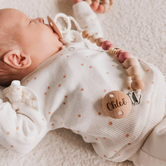 Baby met een gepersonaliseerd roze speenkoord, met naam gegraveerd op de houten clip.